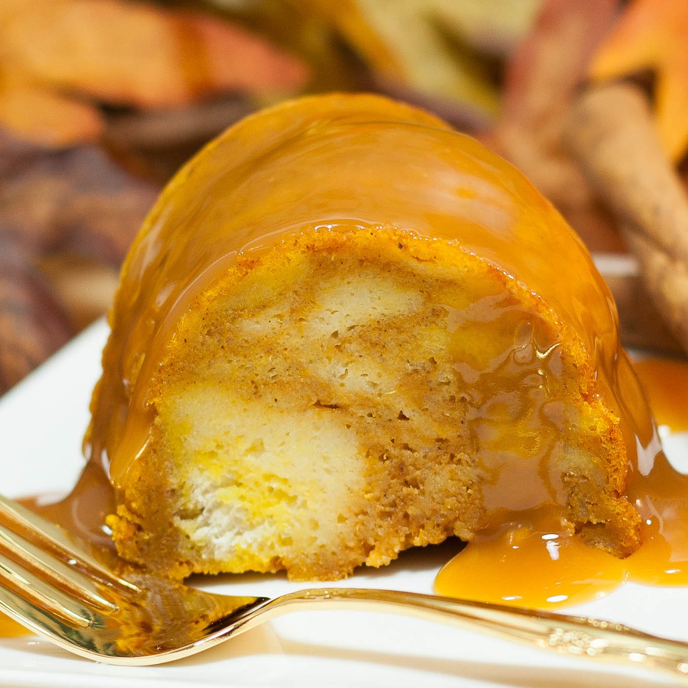 Slice of pumpkin flavored bread pudding covered with caramel sauce. Served on a white plate with gold fork.