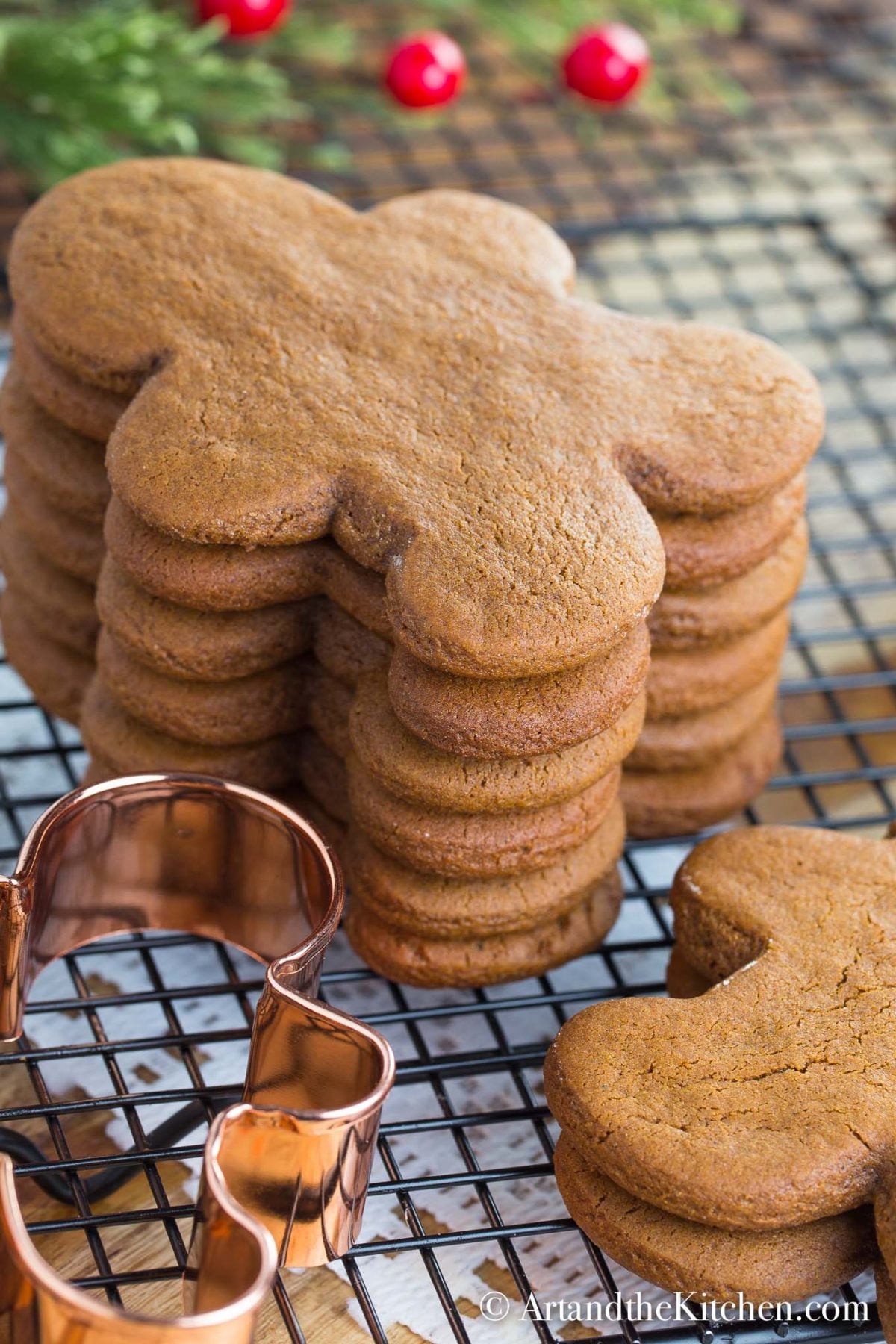 Stack of gingerbread men cookies on cooling rack with copper cookie cutter.