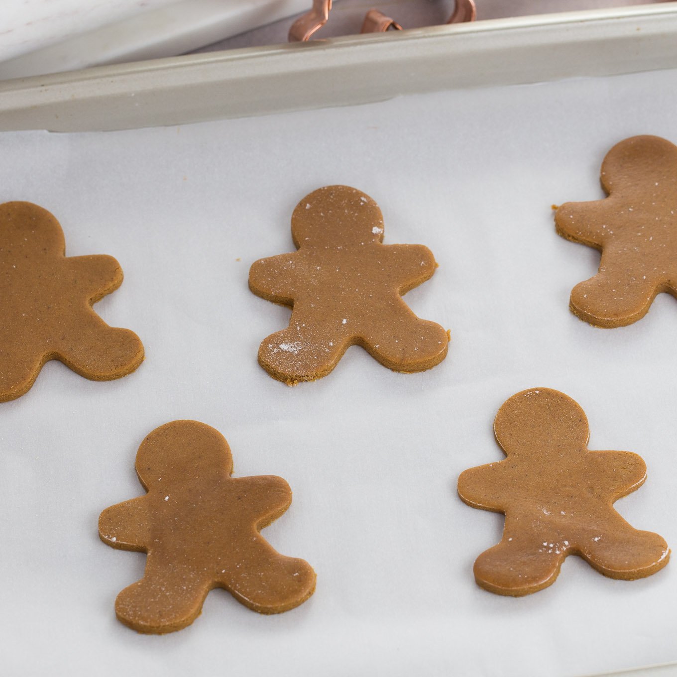 Cut out cookie dough shaped gingerbread men on white parchment line baking sheet.