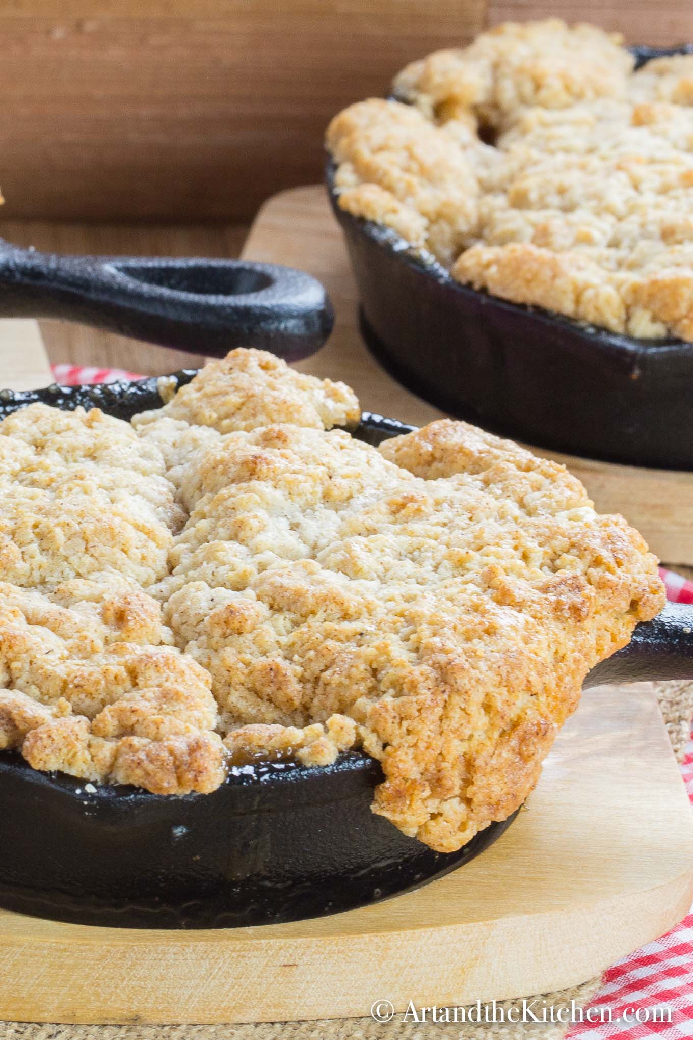 Cinnamon apple filling with a golden brown, buttery crisp topping served in individual cast iron pans on wood plates.
