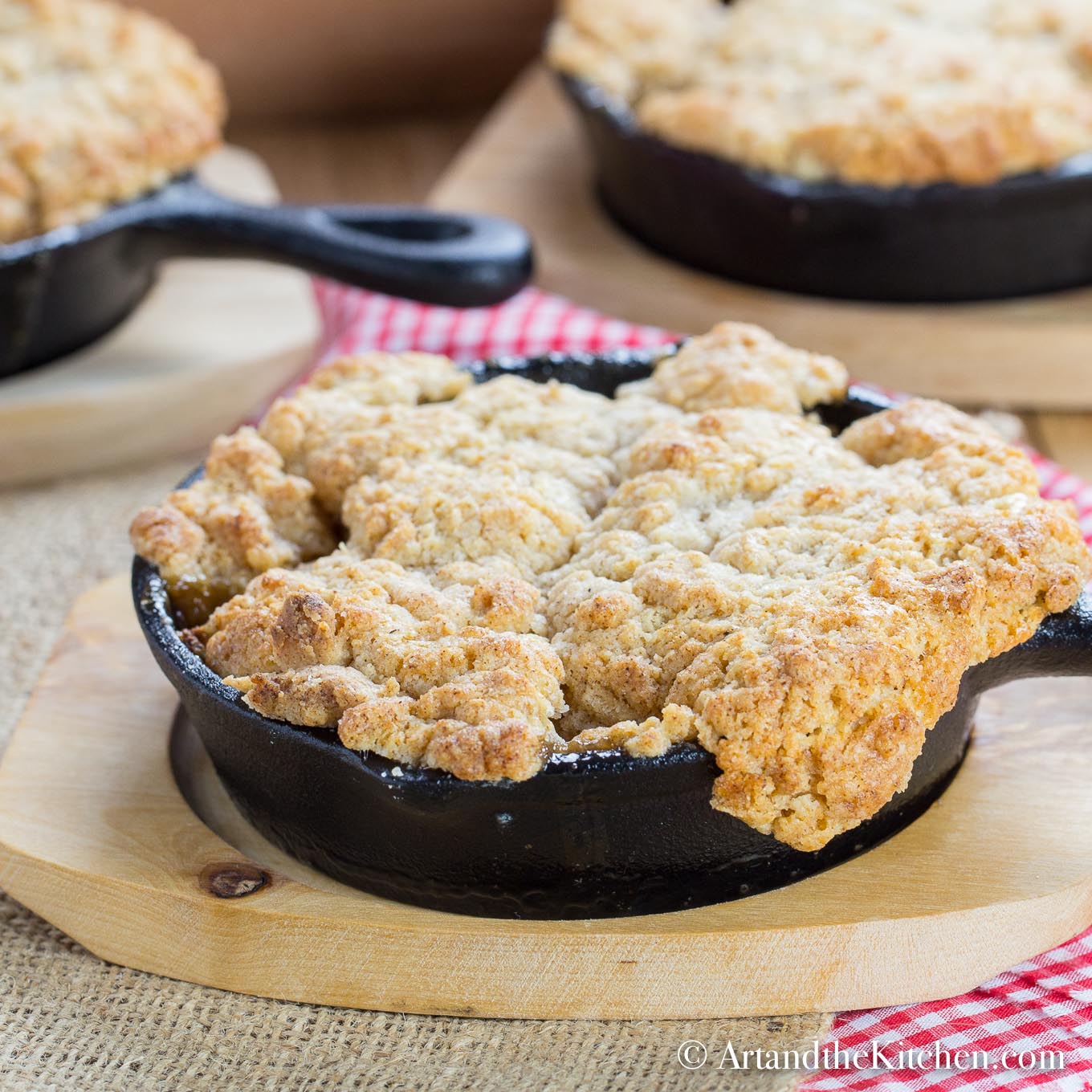 Apple filling with a golden brown, buttery crisp topping served in individual cast iron pan on wood plate.