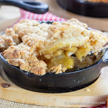 Apple filling with a golden brown, buttery crisp topping served in individual cast iron pan on wood plate.