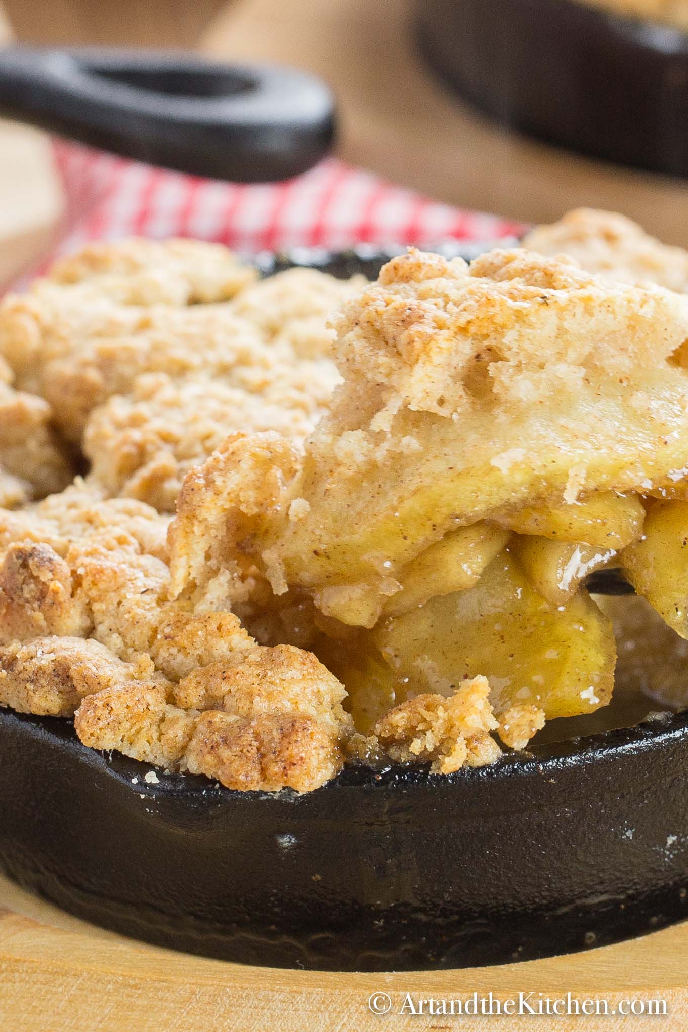 Apple filling with a golden brown, buttery crisp topping served in individual cast iron pan on wood plate.