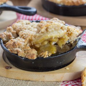 Cinnamon apple filling with a golden brown, buttery crisp topping served in individual cast iron pans on wood plates.