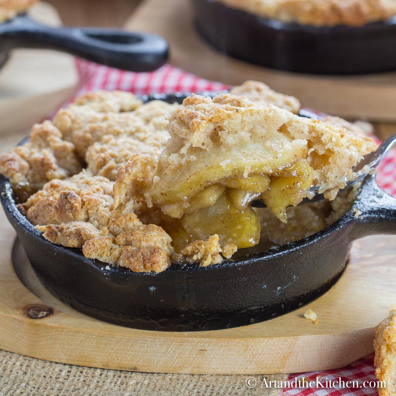 Apple filling with a golden brown, buttery crisp topping served in individual cast iron pan on wood plate.