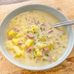 Creamy soup of potatoes and ham in a blue bowl.