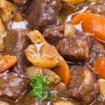 Pot of hearty beef stew with chunks of beef, carrots, mushrooms, and parsley in a rich broth.