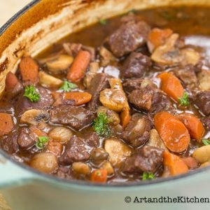 Pot of hearty beef stew with chunks of beef, carrots, mushrooms, and parsley in a rich broth.