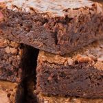 Stack of chocolate brownie squares on white parchment paper.