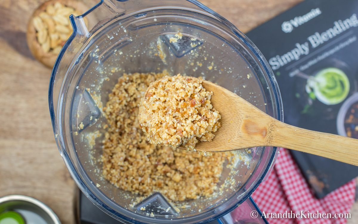 Blender of coarsely ground peanut, dates and coconut. Wooden spoon scooping some out.