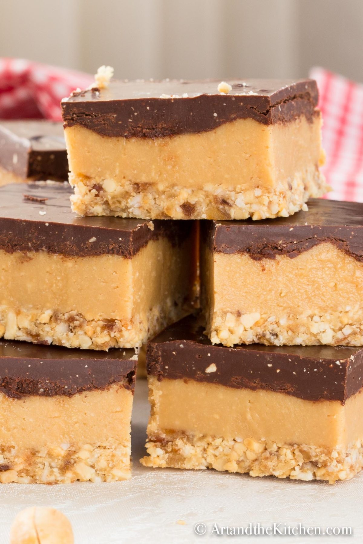 Layered peanut butter bars topped with chocolate and crunchy nuts, stacked.