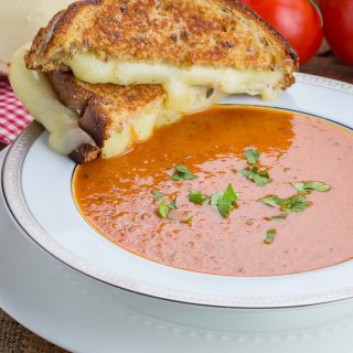 Tomato Soup with grilled cheese sandwich on the side of the bowl.