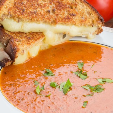 Tomato Soup with grilled cheese sandwich on the side of the bowl.