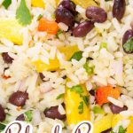 Colorful salad with coconut rice, black bean, pineapple, red peppers, onion, and cilantro on a green plate.