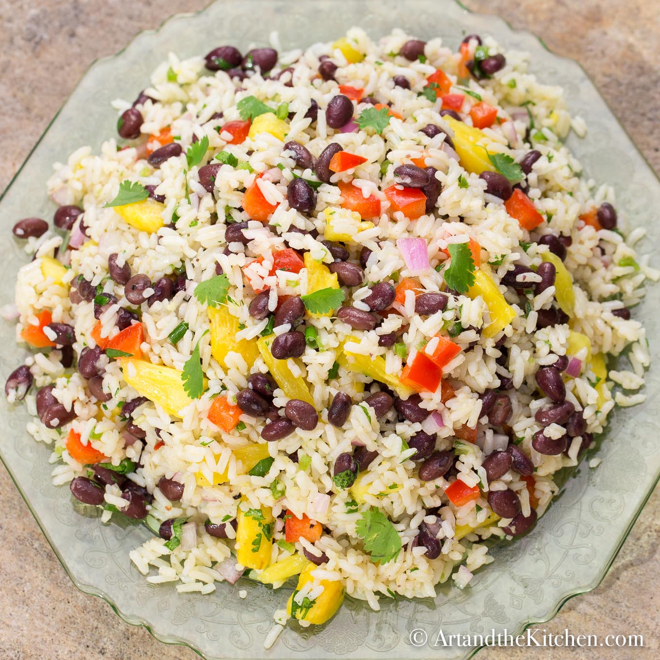 Colorful salad with coconut rice, black bean, pineapple, red peppers, onion, and cilantro on a green plate.