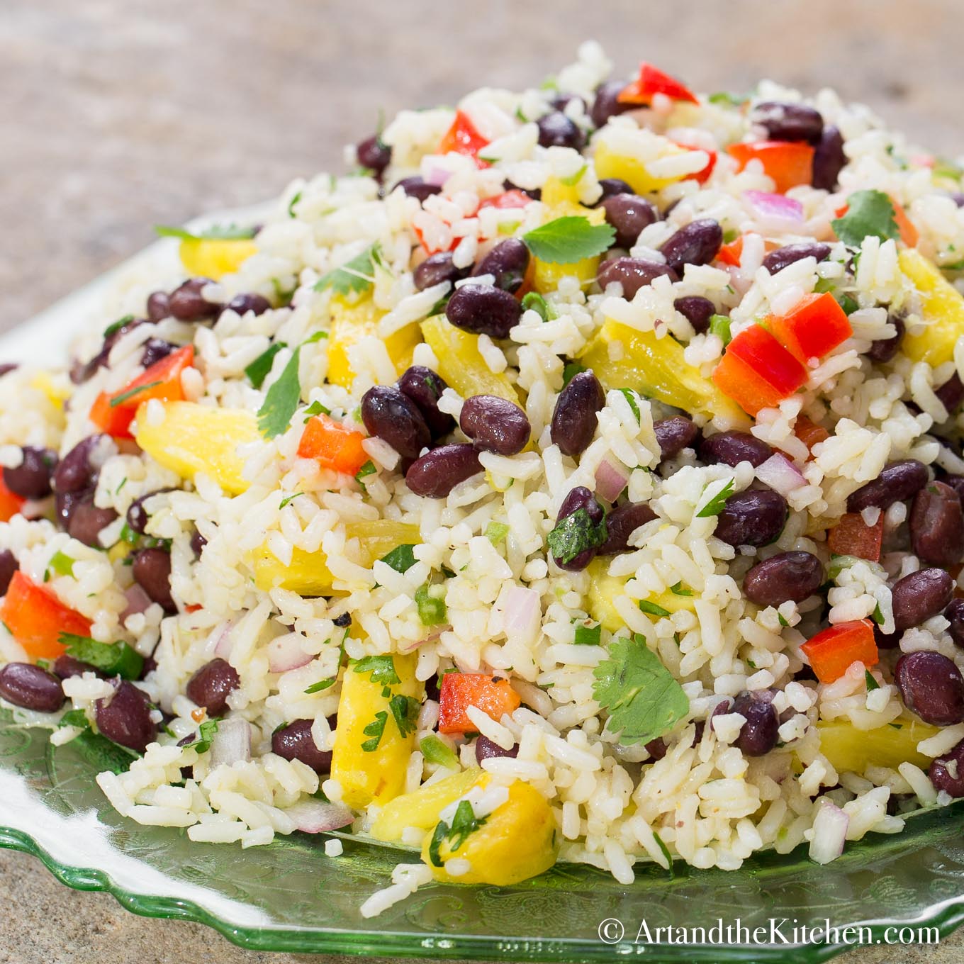 Rice salad beans, pineapple, red peppers, onion, and cilantro on a green plate.