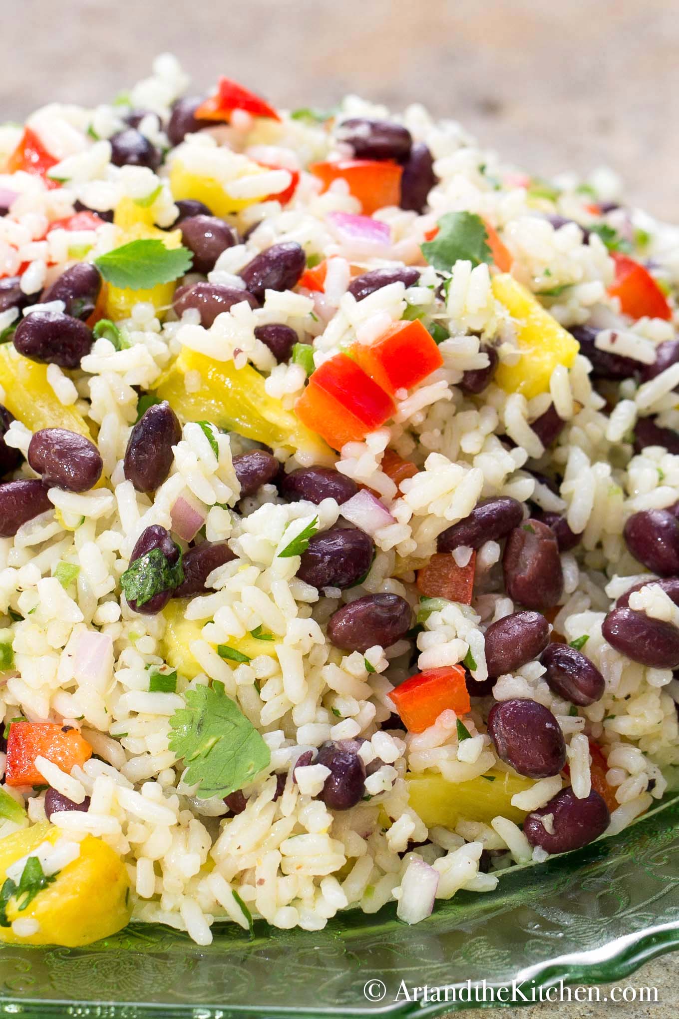 Rice salad beans, pineapple, red peppers, onion, and cilantro on a green plate.