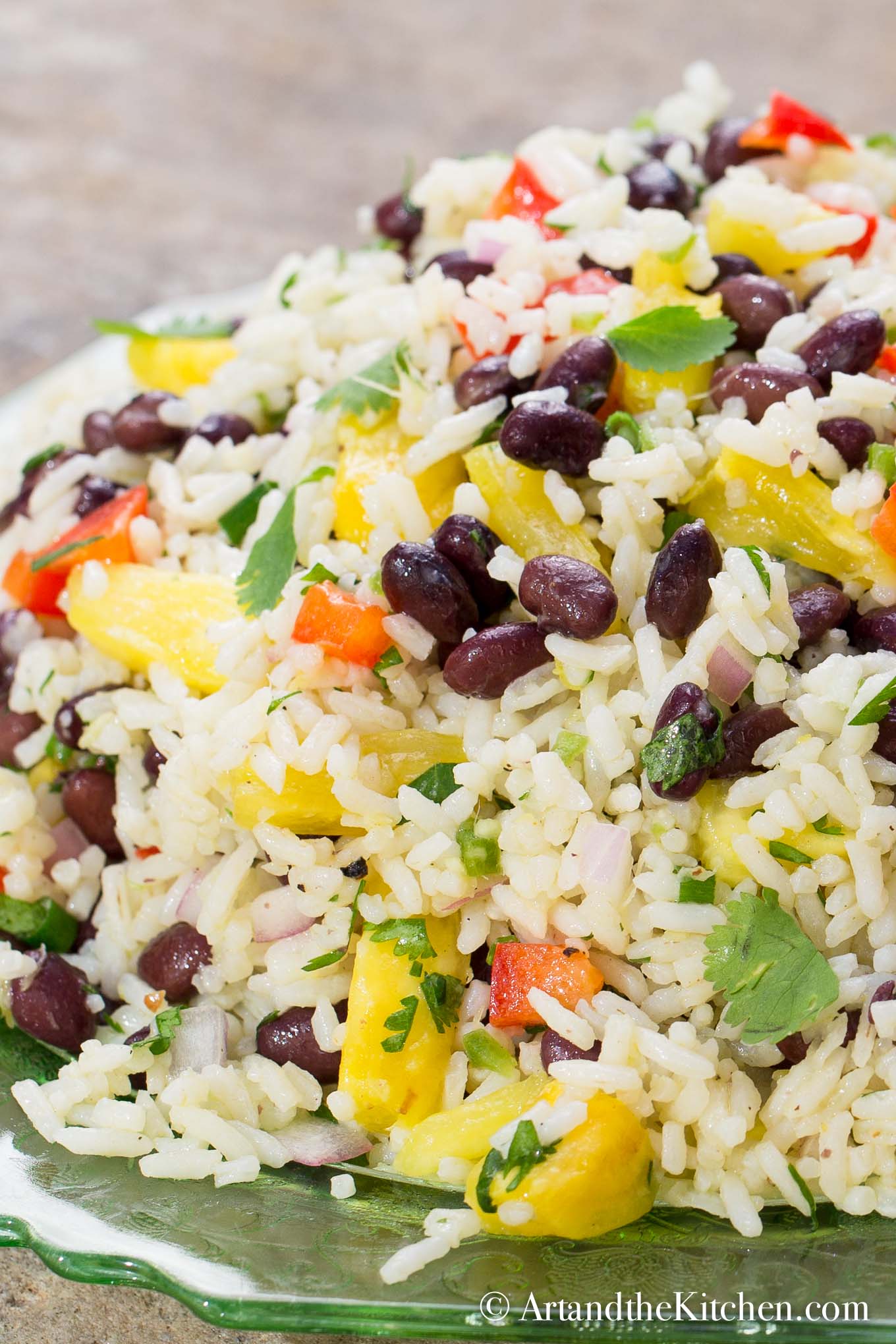 Colorful salad with coconut rice, black bean, pineapple, red peppers, onion, and cilantro on a green plate.