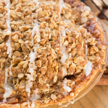 Apple pie in a glass pie plate with a crunchy oatmeal top, drizzled with icing.