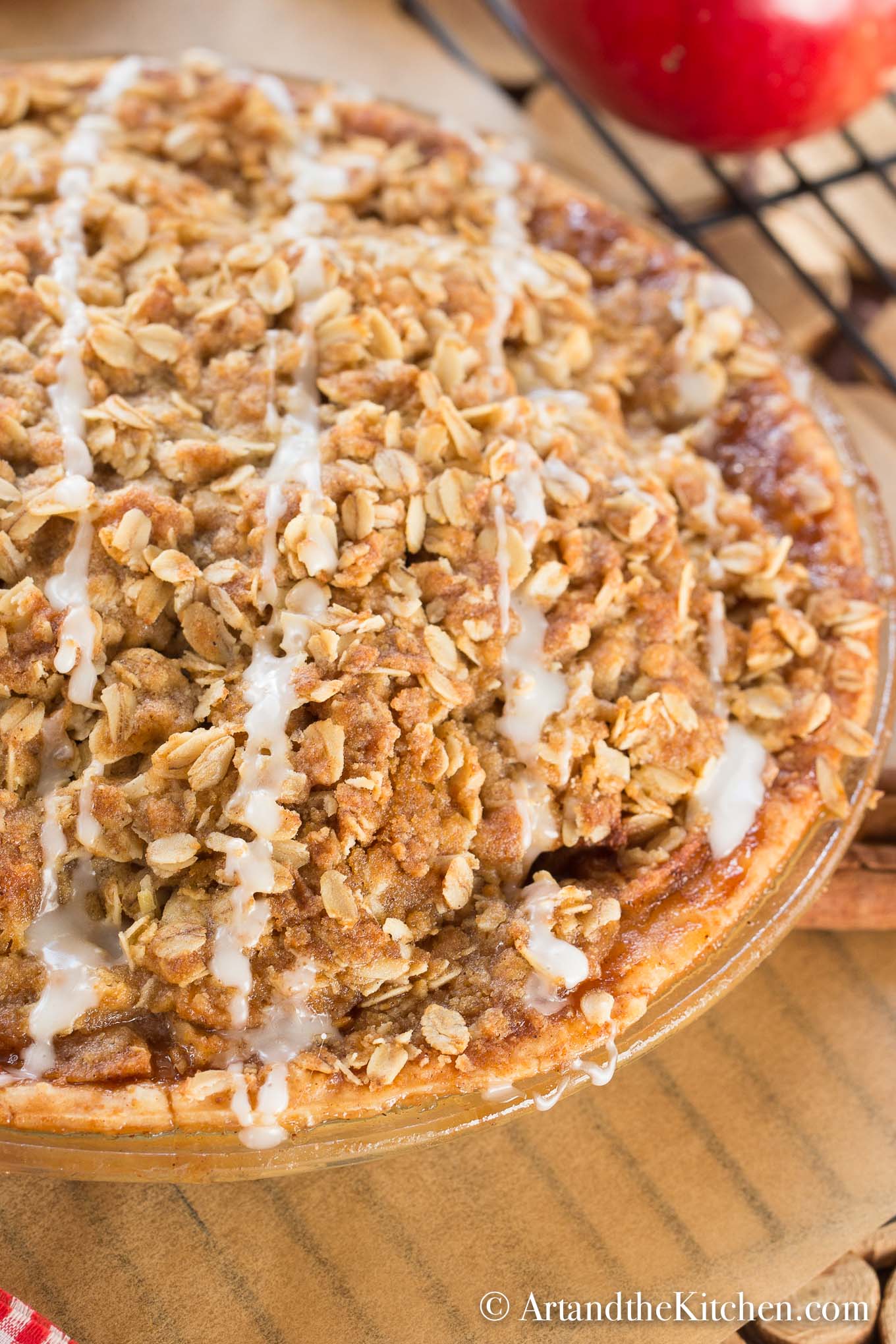 Apple pie in a glass pie plate with a oatmeal crisp top, drizzled with icing.
