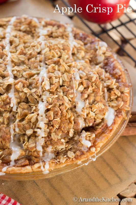 Apple pie in a glass pie plate with a crunchy oatmeal top, drizzled with icing.