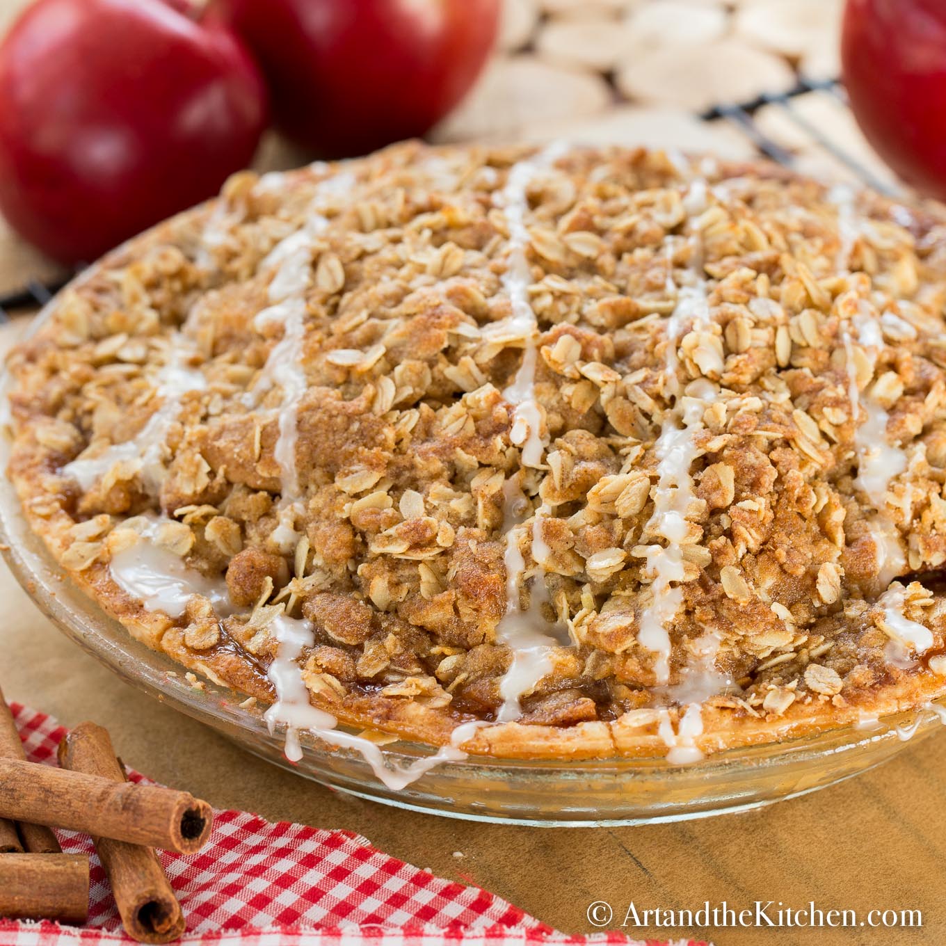 Apple pie in a glass pie plate with an oatmeal topping, drizzled with icing.