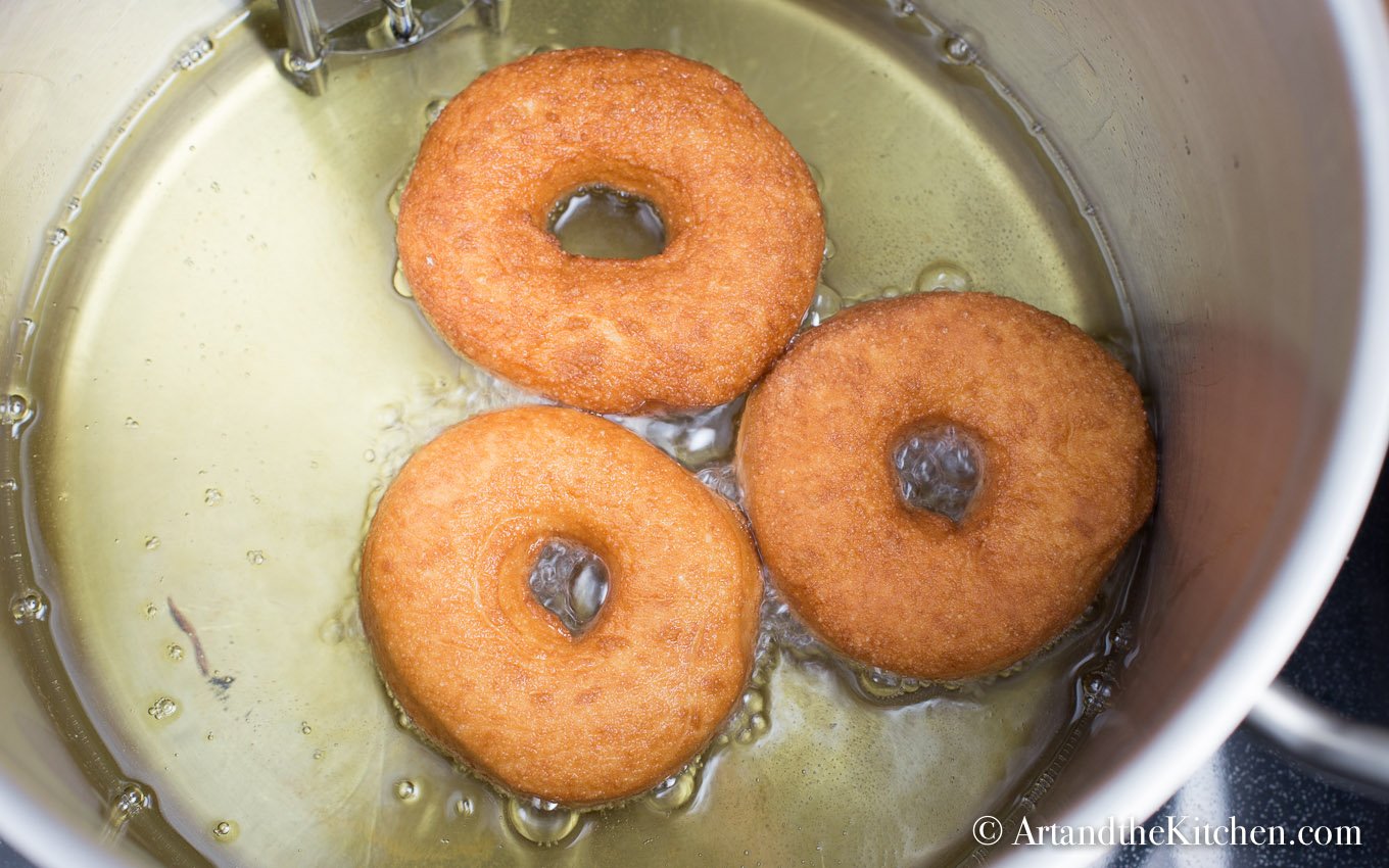 Three donuts frying in pot of cooking oil.