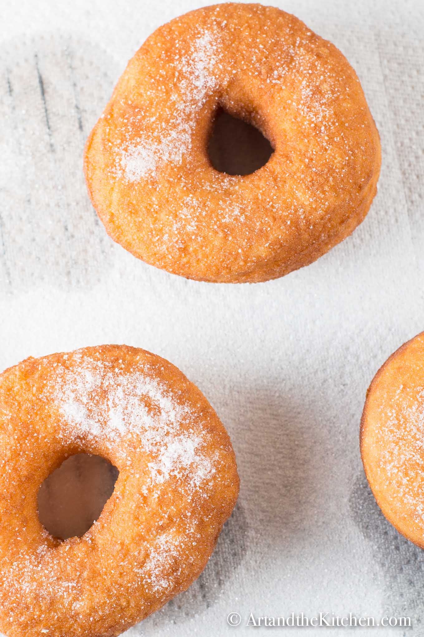 Fresh bread machine donuts sprinkled with sugar on white napkin.