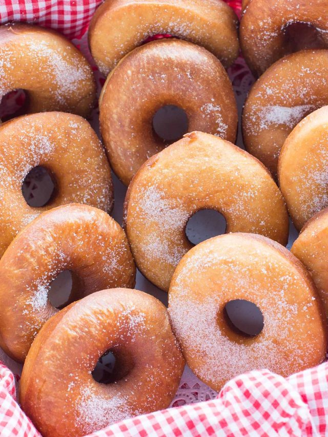 Rows of plain donuts sprinkled with sugar on red checkered napkin.