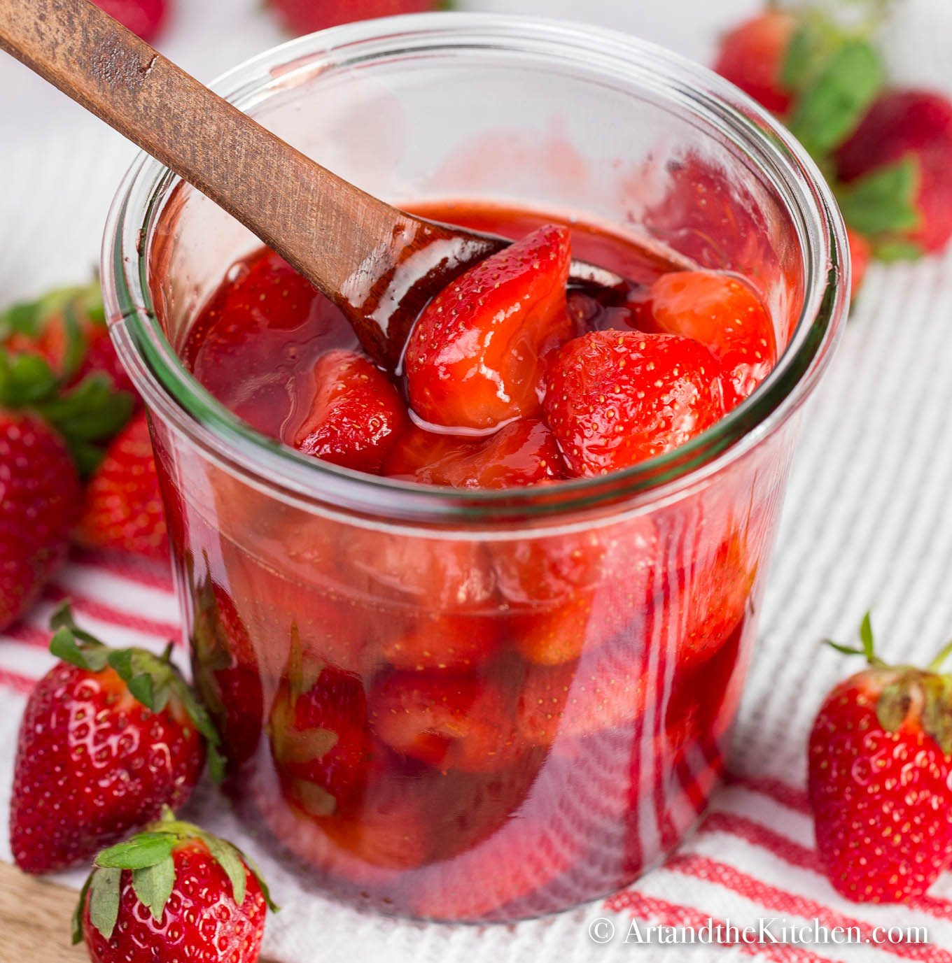 Glass jar filled with homemade strawberry sauce. Wooden spoon scooping sauce out of jar.