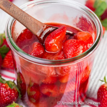 strawberry sauce in glass jar with wooden spoon fresh strawberries in background