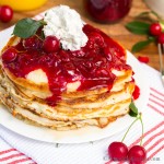 Pancakes stacked and topped with cherry sauce and whipped cream