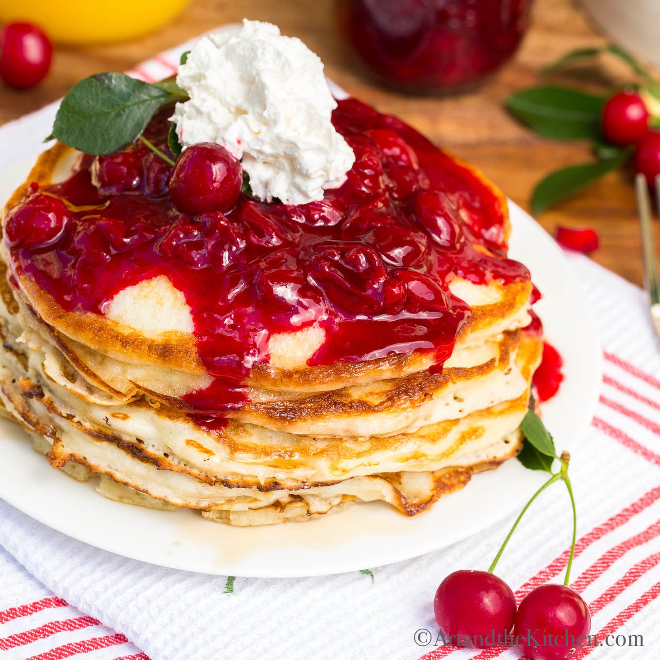 Stack of pancakes topped with cherry sauce and whipped cream.