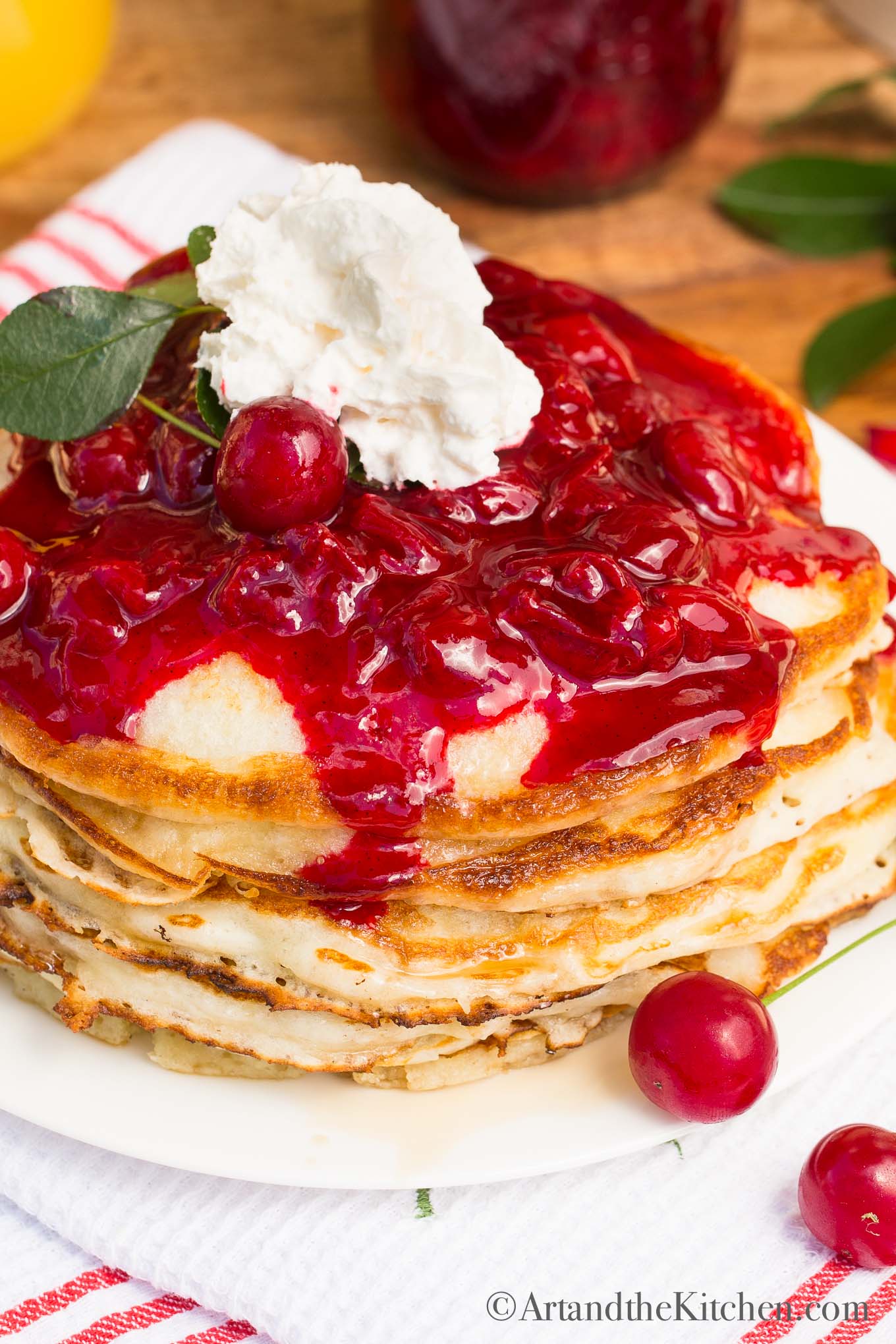 stack of fluffy pancakes topped with cherry sauce and whipped cream