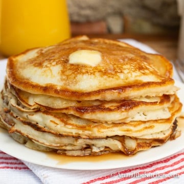 Stack of golden brown pancakes topped with a pat of butter and maple syrup.