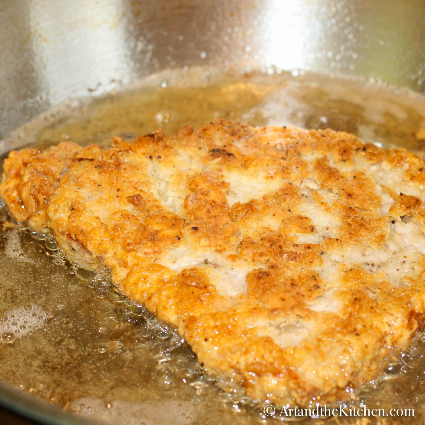 Pork schnitzel frying in oil in stainless steel skillet.