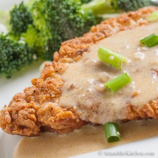 Golden brown fried pork schnitzel topped with a mustard sauce and garnished with green onion slices.