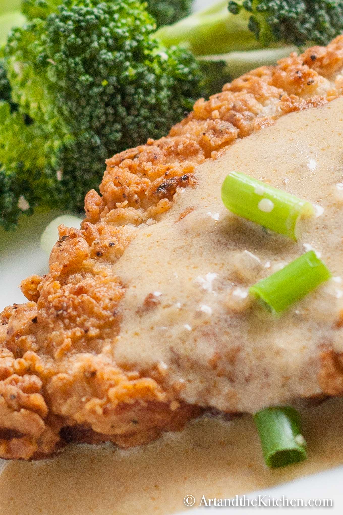 Golden brown fried pork schnitzel topped with a mustard sauce and garnished with green onion slices.