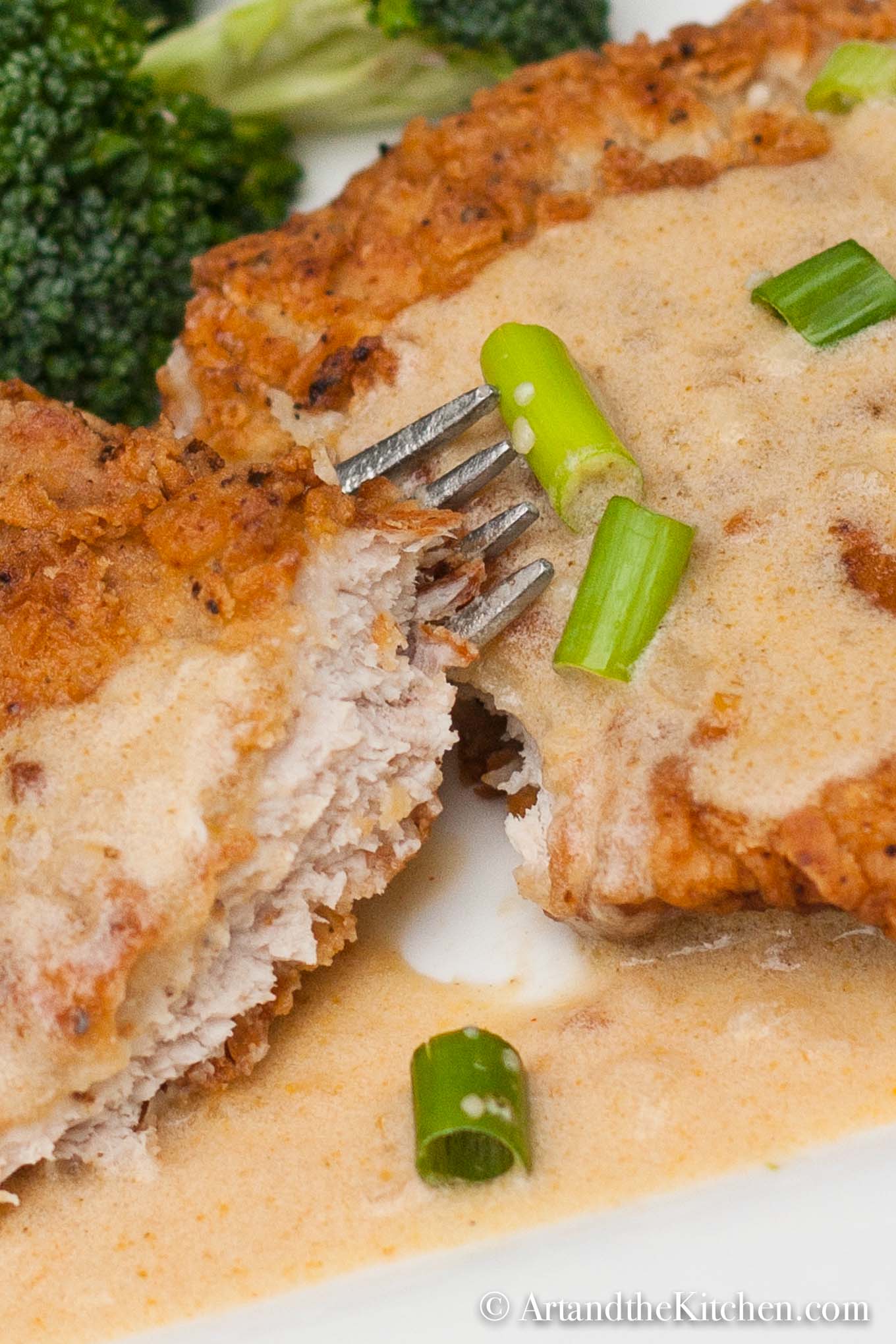 Golden brown fried pork schnitzel topped with a mustard sauce and garnished with green onion slices.