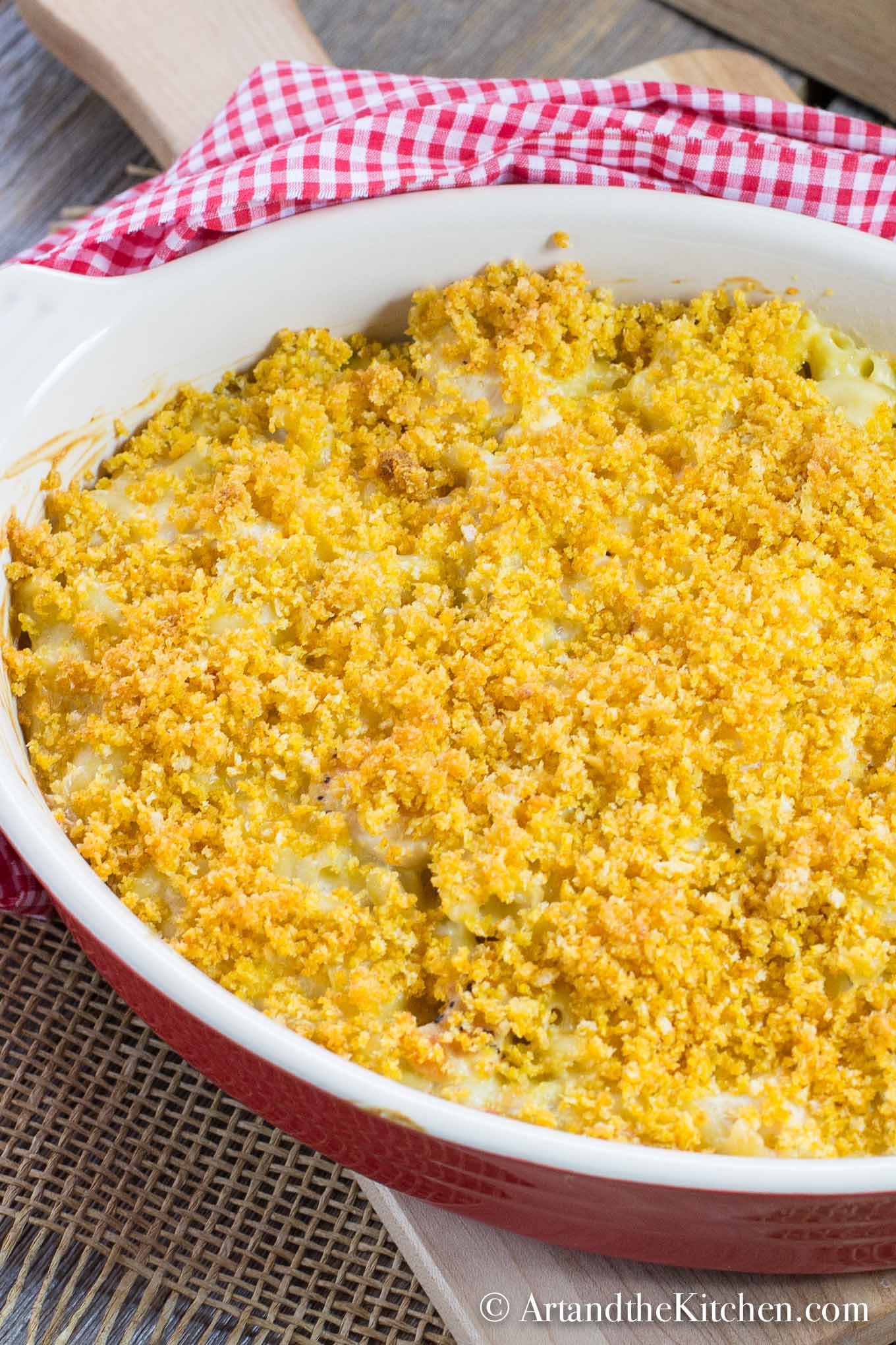 Macaroni casserole with cubes of chicken, golden brown panko bread crumb topping. Served in red stoneware baking dish.