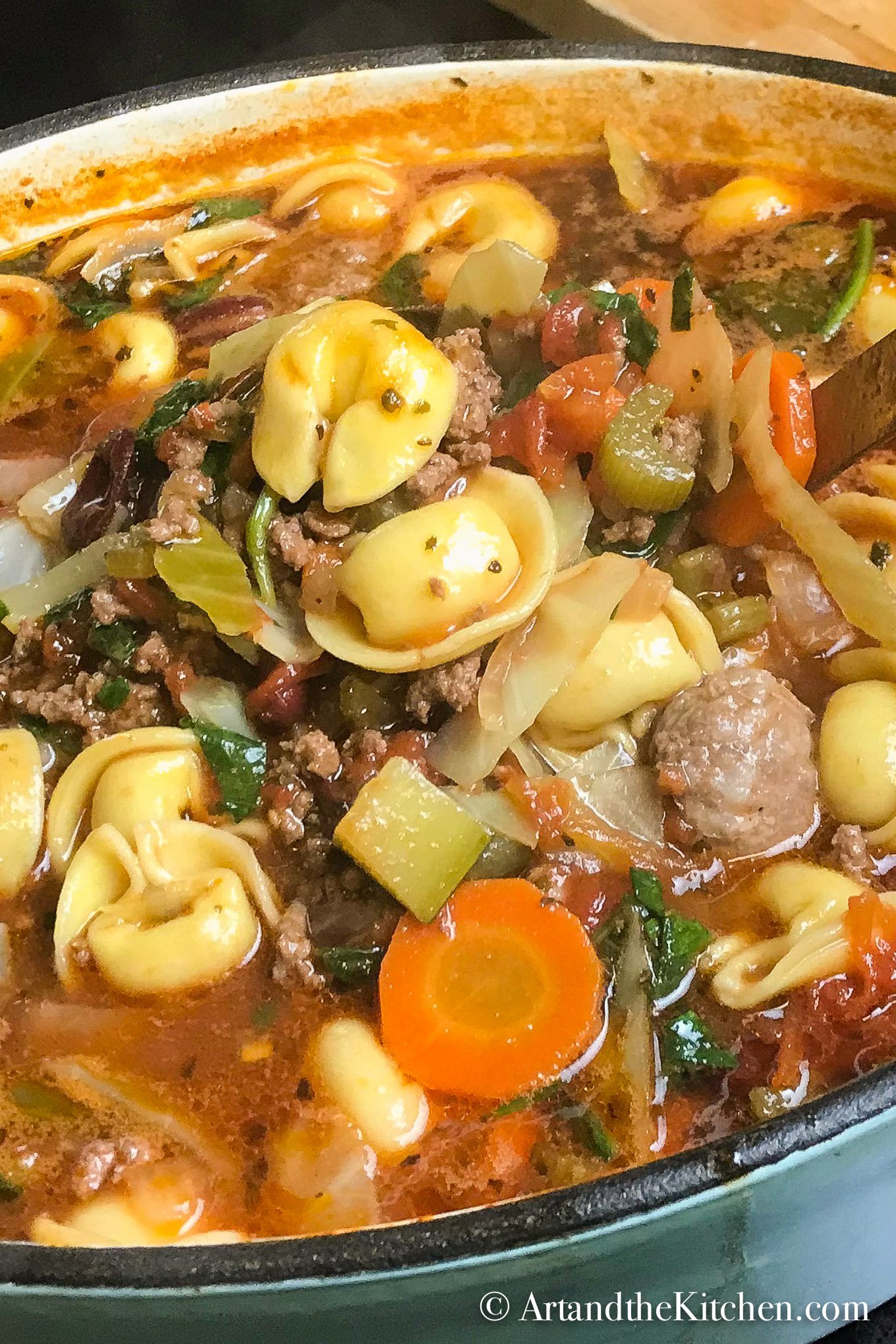 Dutch oven filled with soup of tortellini, vegetables, sausage and ground beef.
