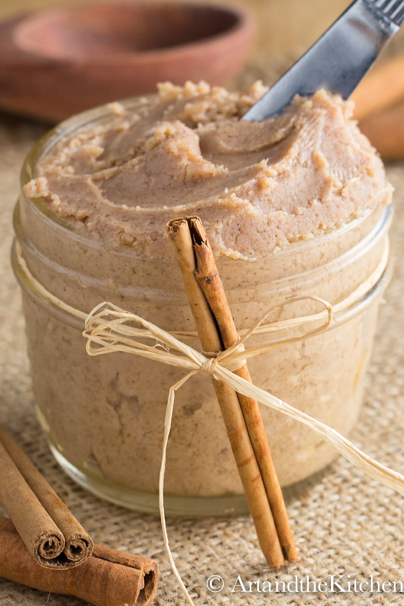 Small glass jar decorated with a ribbon and cinnamon stick, filled with cinnamon butter.