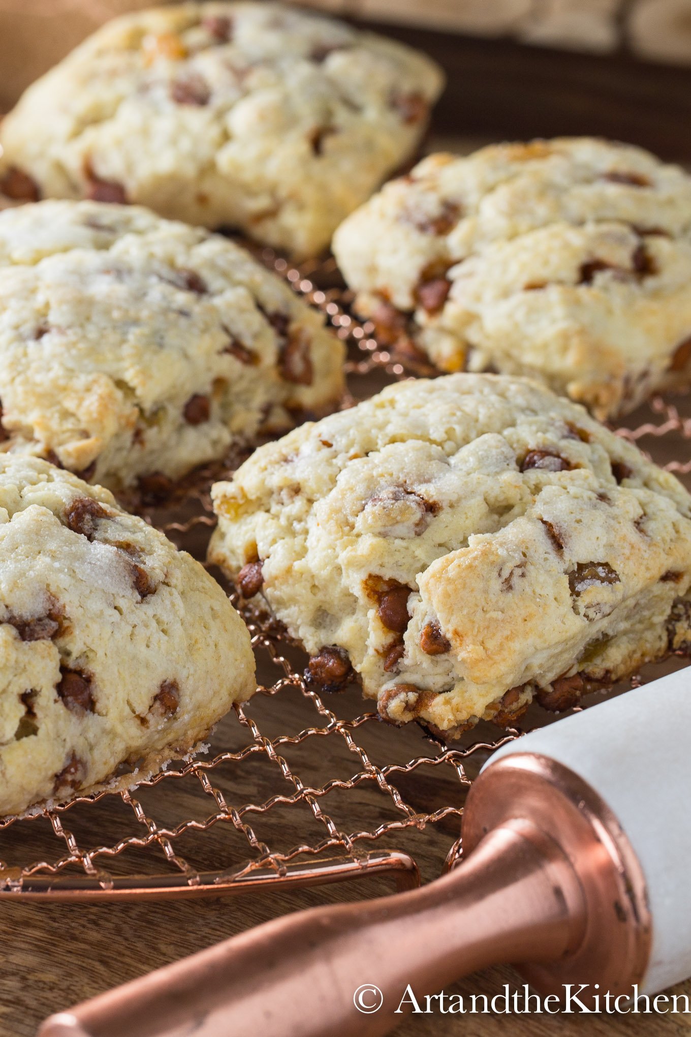 Cinnamon and raisin scones on a copper cooling rack with decorative rolling pin