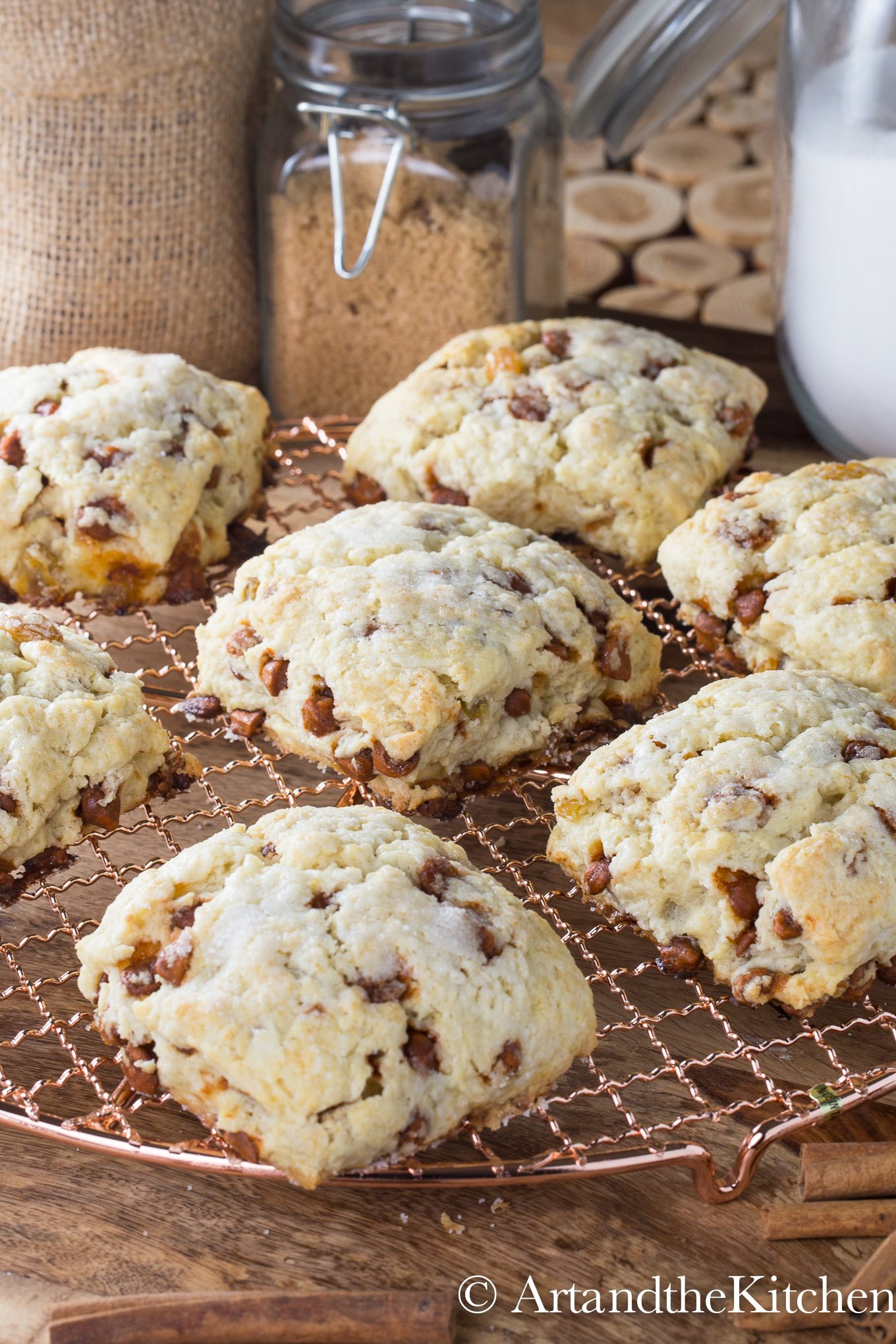 Cinnamon and raisin scones on a copper cooling rack with decorative jars of sugar in the background