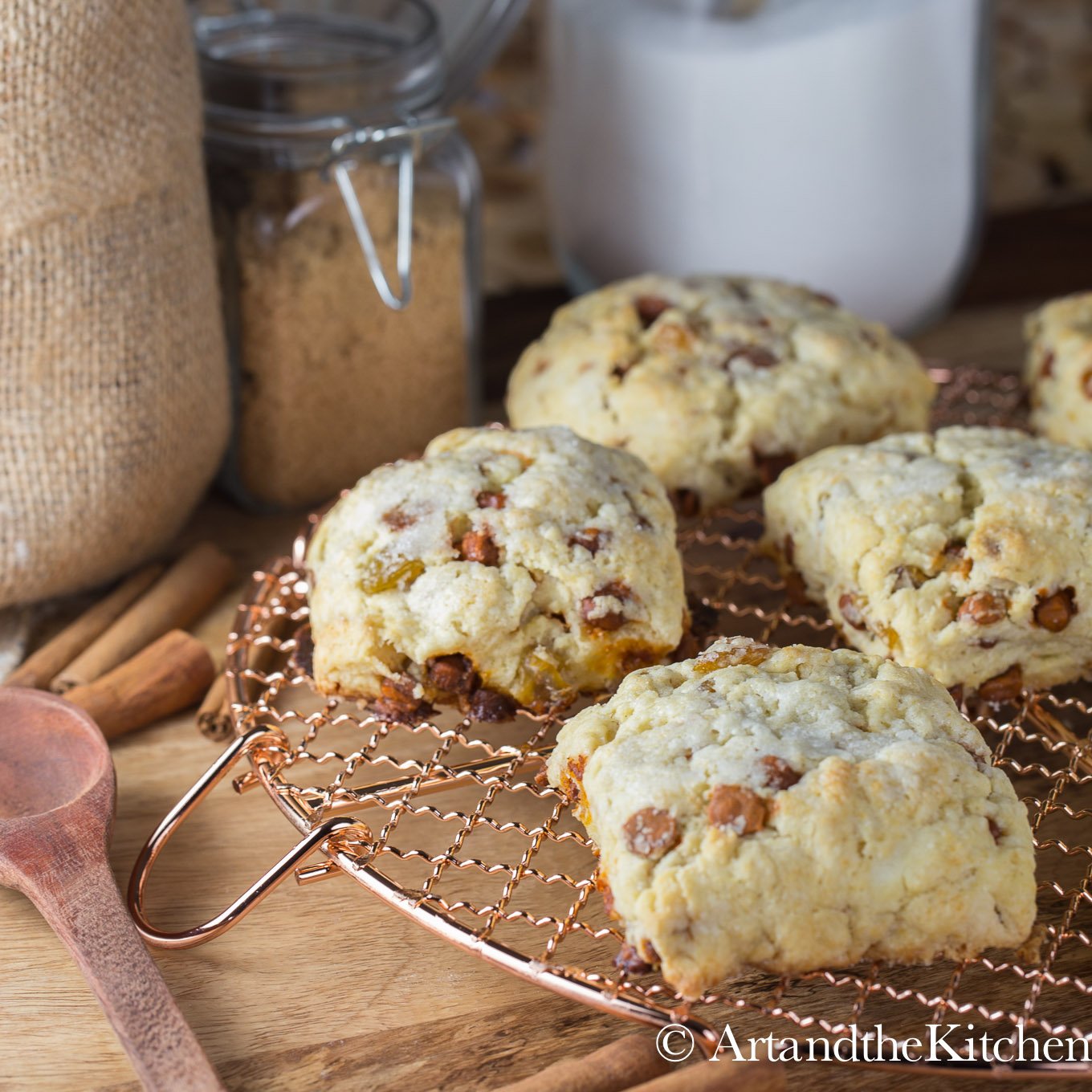 Cinnamon and raisin scones on a copper cooling rack with decorative jars of sugar in the background