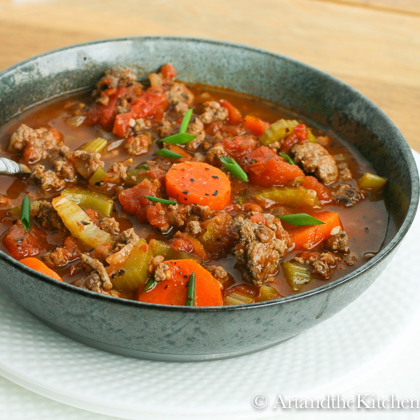 Green bowl filled with soup made with chunks of ground beef, carrots, tomatoes and celery.