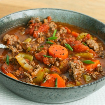 Green bowl filled with soup made with chunks of ground beef, carrots, tomatoes and celery.