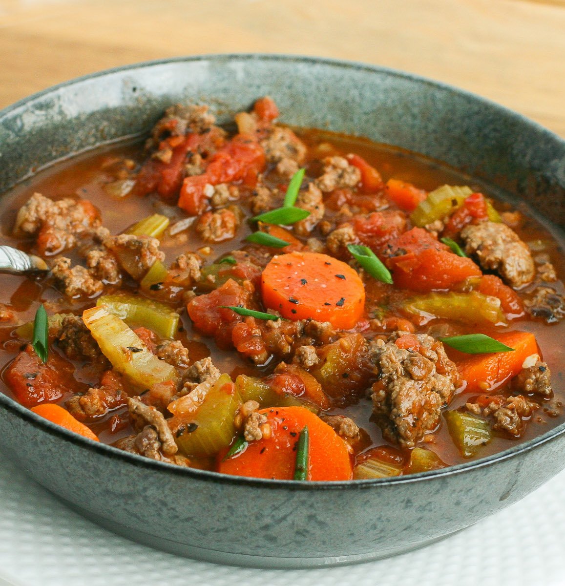 Green bowl filled with soup made with chunks of ground beef, carrots, tomatoes and celery.