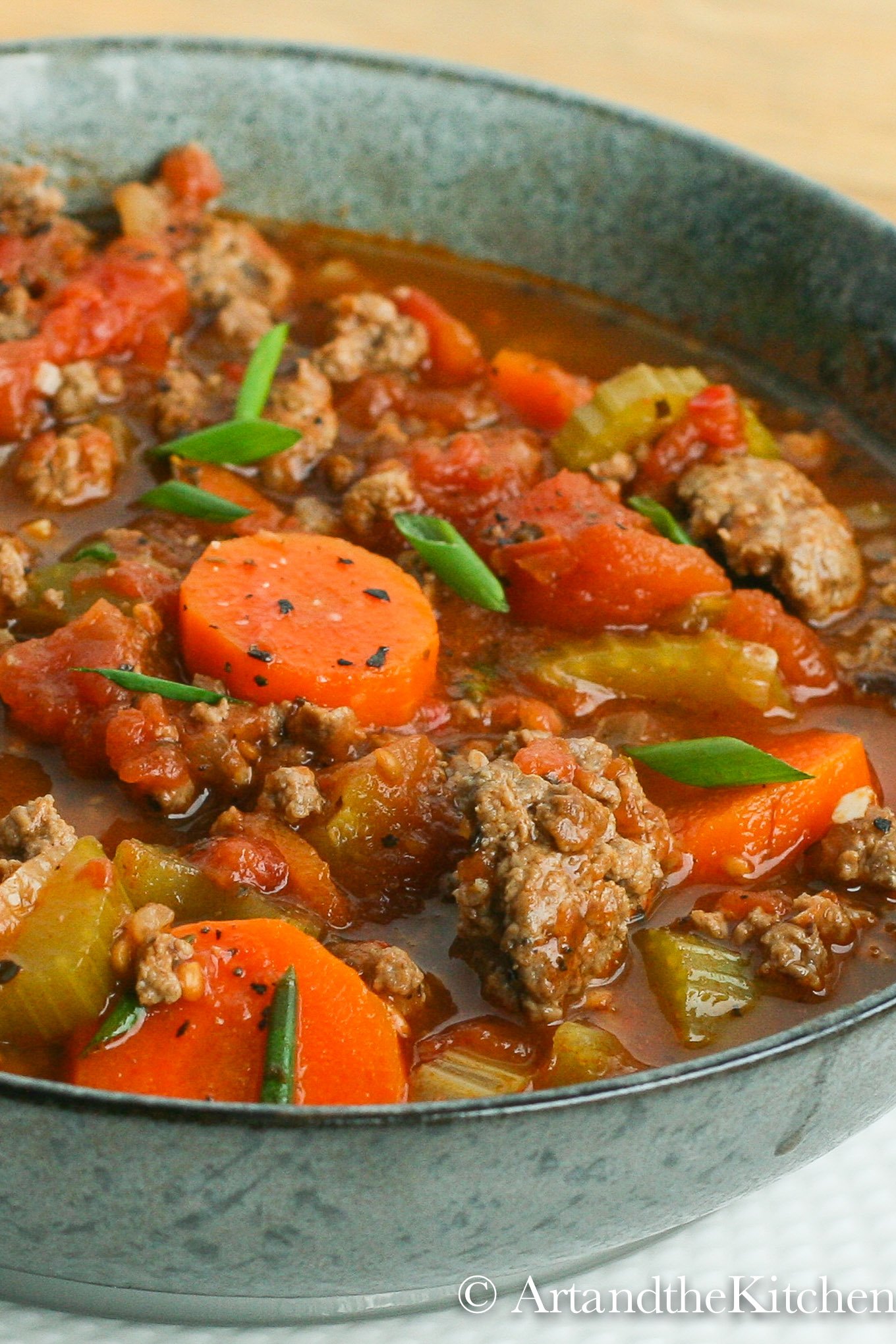 Green bowl filled with soup made with chunks of ground beef, carrots, tomatoes and celery.