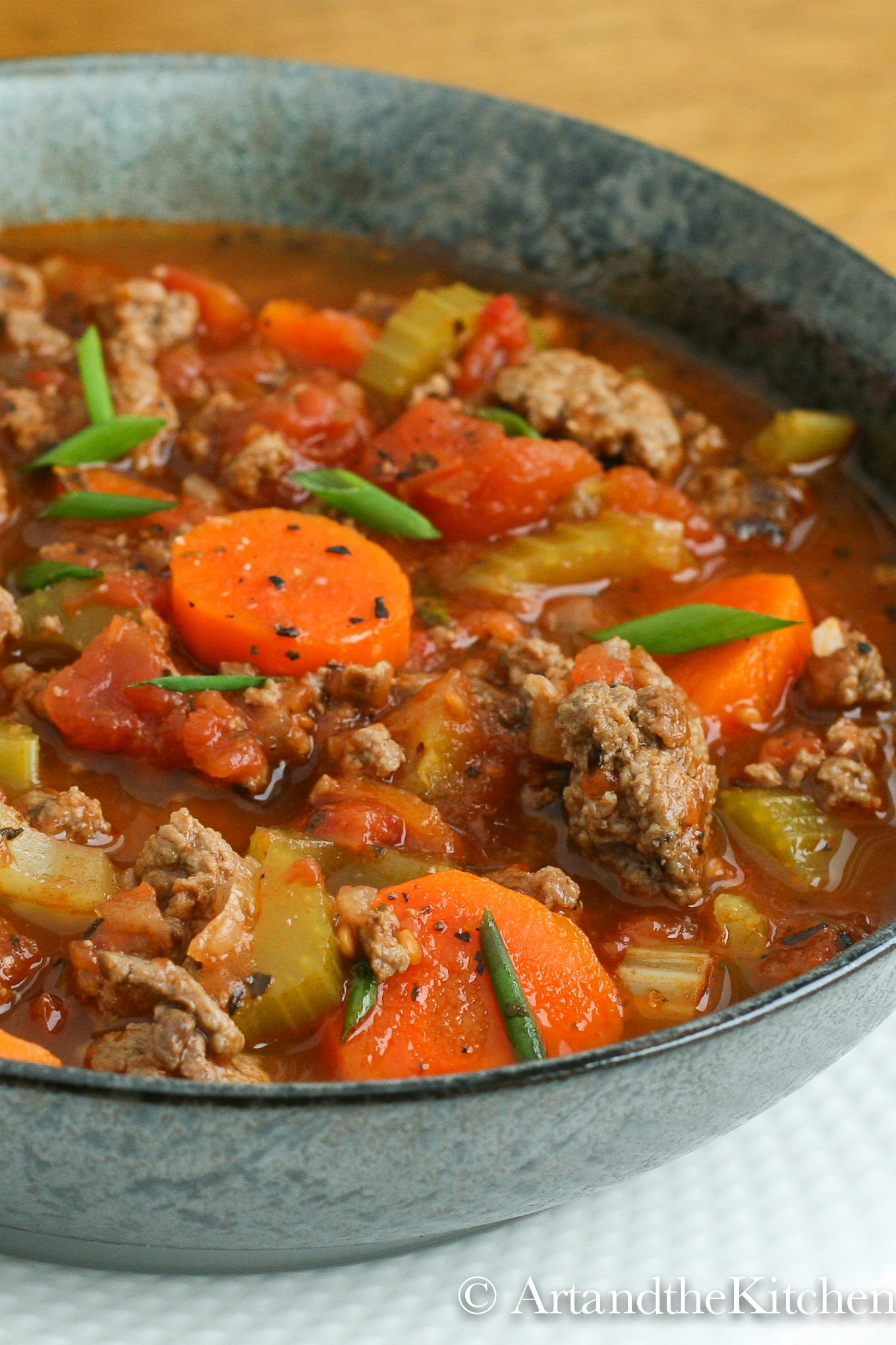 Green bowl filled with soup made with chunks of ground beef, carrots, tomatoes and celery.